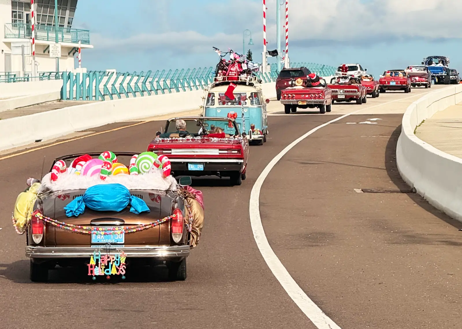 Classic cars crossing the drawbridge in the parade: a convertible piled with giant candy, a red convertible and a VW bus leading a line of classics