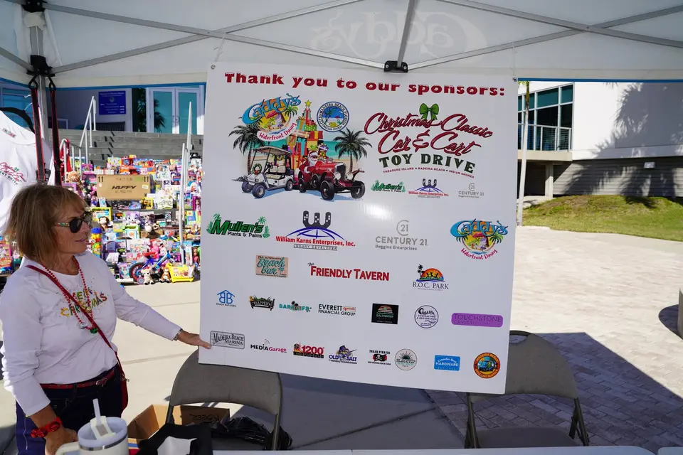 Volunteer beside the printed thank-you-to-our-sponsors board