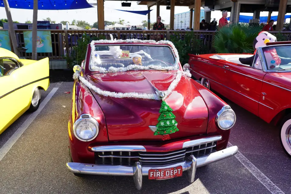 Maroon Studebaker with a Christmas tree on the hood and a FIRE DEPT plate, parked among classic cars at the lineup